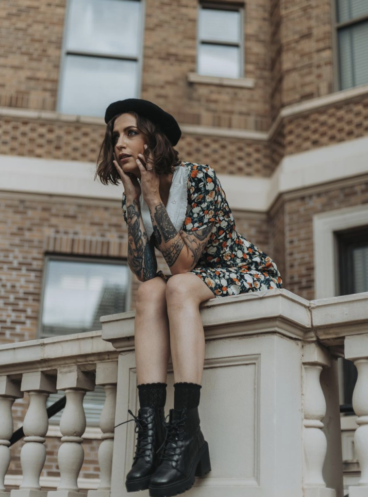 A woman with tattoos sitting on a ledge.
